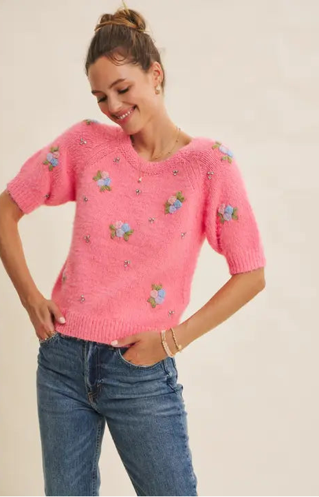 Woman wearing a pink knitted sweater with floral patterns and blue jeans on a beige background