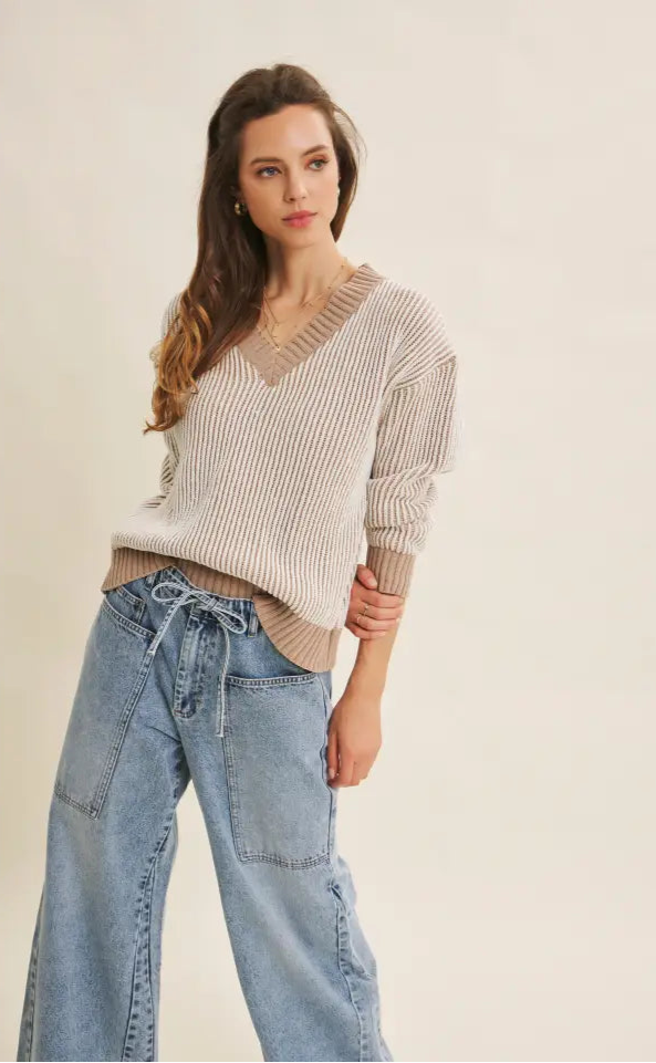 Woman wearing a beige sweater and blue jeans against a plain background