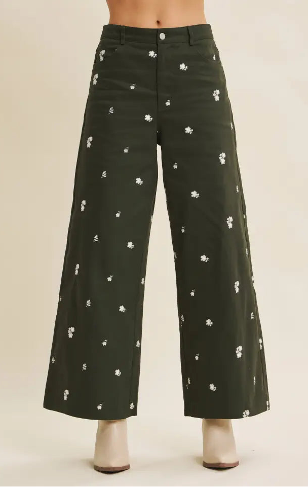 Dark green pants with white floral pattern worn by a person on a beige background